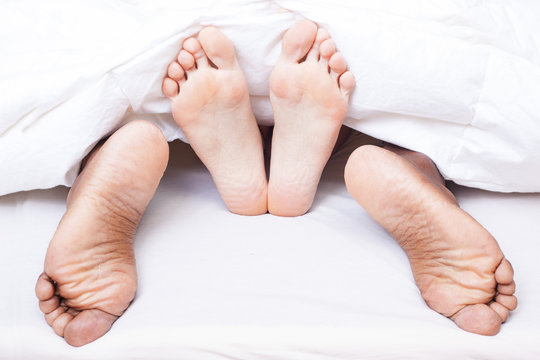 Black and white feet of interracial couple in bed