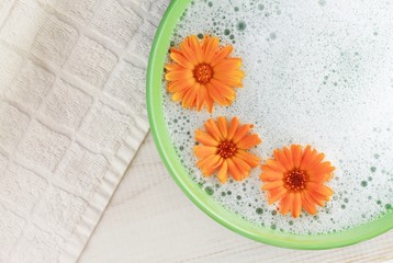 Soothing cleansing foam bath with calendula. Bright flowers, aromatic foam in green bowl, white towel background. Top view. 
