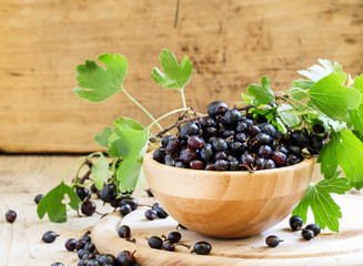 Black currant in bowl, vintage wooden background, selective focu