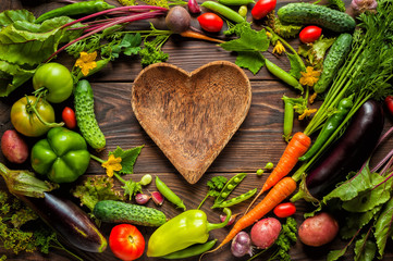 Plate heart shape surrounded with Fresh organic Vegetables on Wooden Background. Healthy Vegetarian...