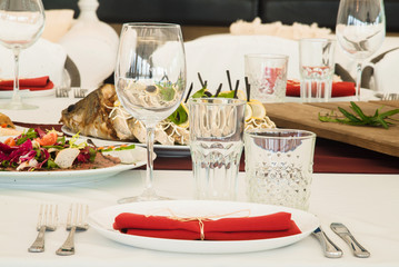Red napkins, white plates and tablecloth, glasses, forks, knives, spoons and flower composition on served banquet table