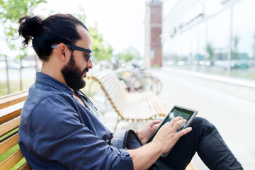 man with tablet pc sitting on city street bench
