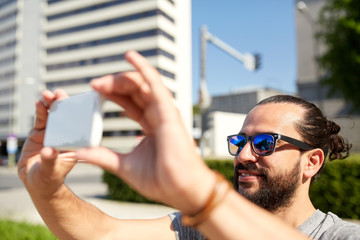 man taking video or selfie by smartphone in city