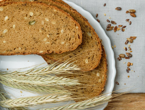 Fresh crusty bread on the plate and wheat ears at wooden table