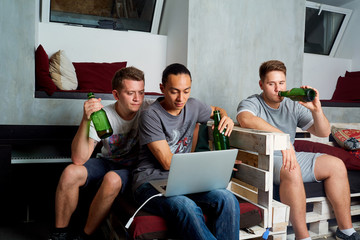Friends together looking at a laptop and drinking beer in the ro