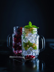 Fresh berries with ice in mason jar on dark background