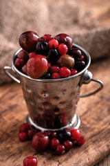 Small metal pail with different berries on wooden table