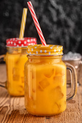 Fresh orange juice with ice in a mason jar on wooden table.