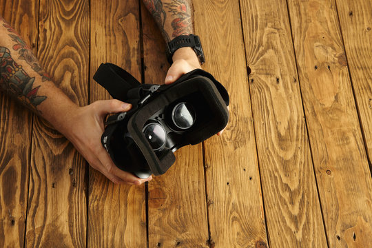 Tattoed hands hold vr glasses upside down, presentation of new technology