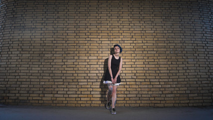Fototapeta na wymiar Street youth movements and styles. Beautiful girl in a black dress on brick wall background.