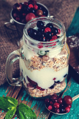 Muesli, fresh berries and yogurt in glass mason jar on wooden table