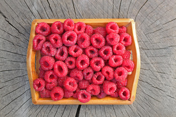 Fresh raspberries in little wooden tray on stump