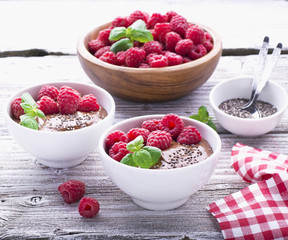 Chocolate banana smoothies with chia seeds served ripe raspberries and fresh mint on a light wooden background. The white ceramic bowls of serving  healthy breakfast