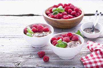 Chocolate banana smoothies with chia seeds served ripe raspberries and fresh mint on a light wooden background. The white ceramic bowls of serving  healthy breakfast