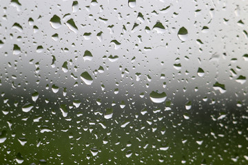 Water raindrop on window glass with green meadow and gray sky