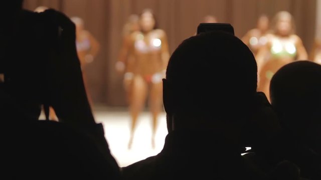 Silhouettes of cameramen photographing beautiful fitness models posing in bikini