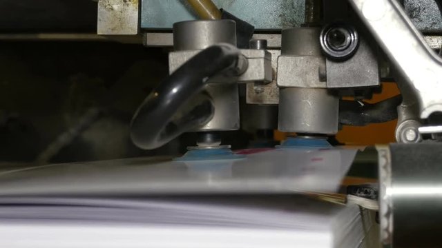 Vacuum sheet feeder supplies individual sheets of paper into printing press from the pile of paper. Related to machinery, technology of printing. Extreme closeup. 4K Ultra HD.