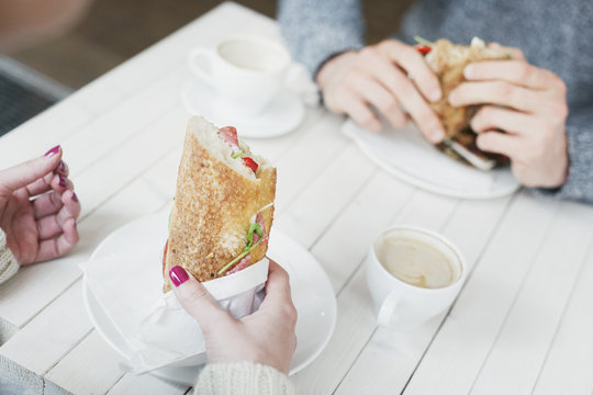 Cropped image of friends holding sandwiches at cafe table