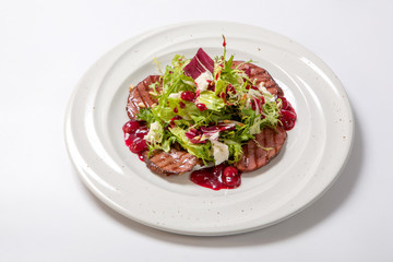 Salad with grilled veal and fresh salad leaves with cherry sauce on a white plate