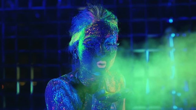 girl in ultraviolet light blows green fluorescent powder with palm