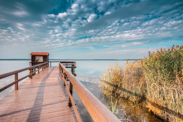 Fototapeta na wymiar Old wooden pier for fishing, small house shed and beautiful lake
