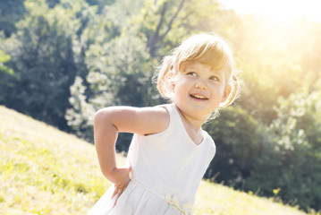 Fototapeta na wymiar Portrait of adorable little girl in white dress smiling in a meadow.