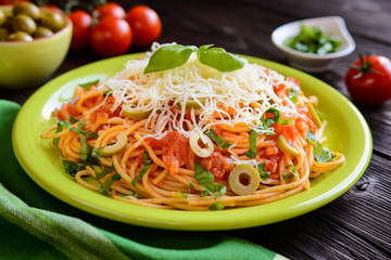 Spaghetti pasta salad with tomato sauce, olives, Gouda cheese and basil on a wooden background 