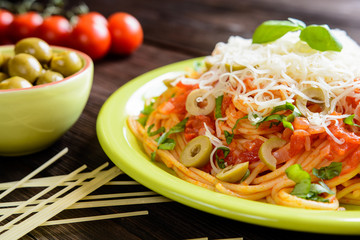 Spaghetti pasta salad with tomato sauce, olives, Gouda cheese and basil on a wooden background 
