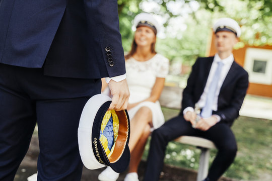 Midsection of graduate holding cap while friends sitting on bench at party