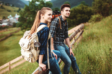 A couple of tourists sitting on a wooden fence and view beautiful countryside. The concept of active rest