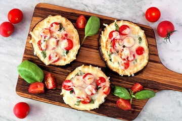 Healthy eggplant mini pizzas with melted mozzarella, tomatoes and basil on a serving board against...