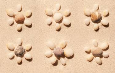 Fototapeta na wymiar Six flowers made of sea stones on sand