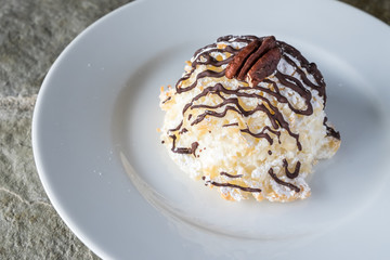 Coconut macaroon drizzled with chocolate on a white plate, highlighted by the sun
