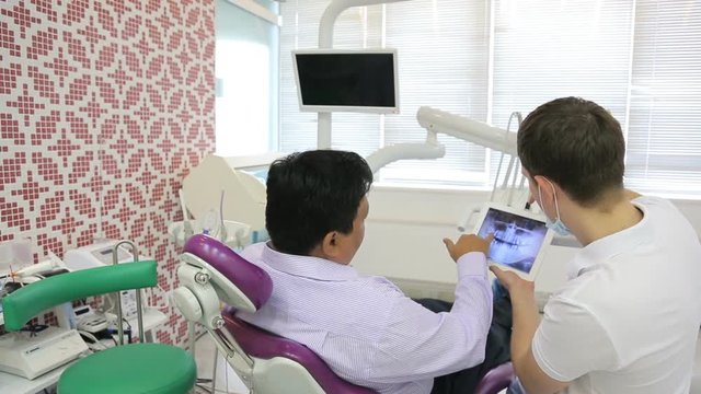 Dentist and patient man, discuss treatment with your tablet with x-ray image.