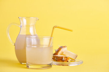 Glass and jug of fresh pineapple juice on yellow