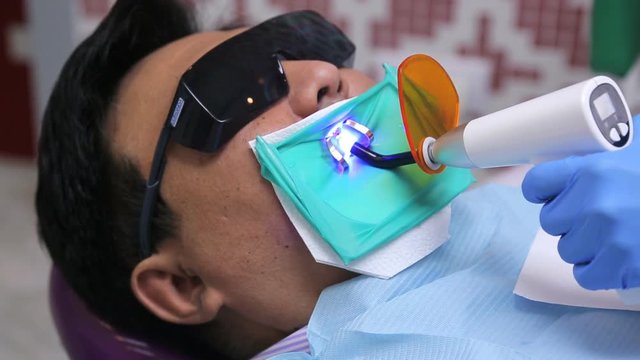 Hand of dentist holding an LED lamp in oral cavity of patient with glasses from ultraviolet.