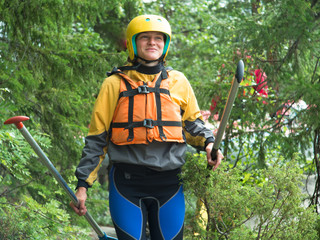 Young woman walking through the woods with two paddles and a helmet