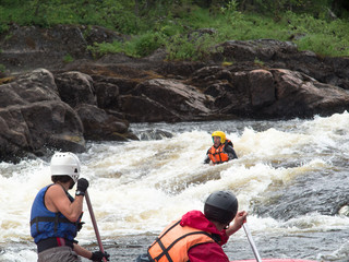 Two rowers on the catamaran trying to save a drowning man in the river with rapids