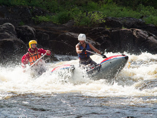 Two friends on an inflatable catamaran ride on the rough river with splashes