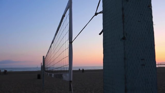 Cool shot of volleyball net at a beach during sunset hours with people riding bikes in the background closer to the ocean