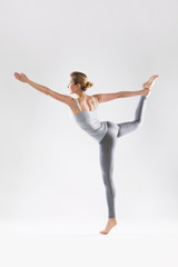 Beautiful young woman doing yoga on a gray studio background