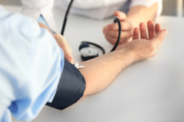 Female doctor measuring man blood pressure with tonometer - obrazy, fototapety, plakaty