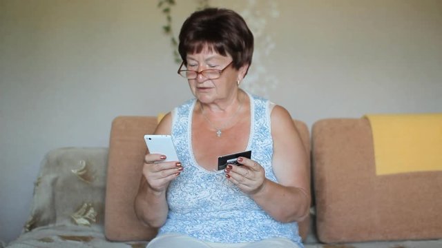 Happy mature woman using credit card and phone at home