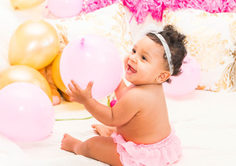 Fototapeta na wymiar Baby Girl Sitting With Pillows and Balloons