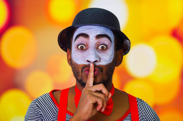 Headshot pantomime man with facial paint posing for camera using hands to cover mouth, blurry...