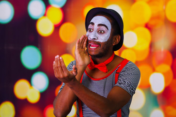 Pantomime man with facial paint posing for camera holding blowing horn, blurry lights background