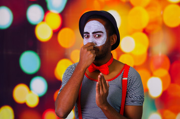 Pantomime man wearing facial paint posing for camera, using hands interacting body language, blurry...