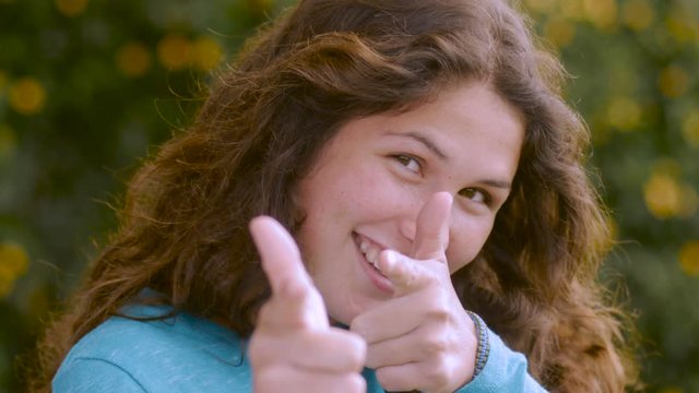An young woman points with both hands at the camera and winks