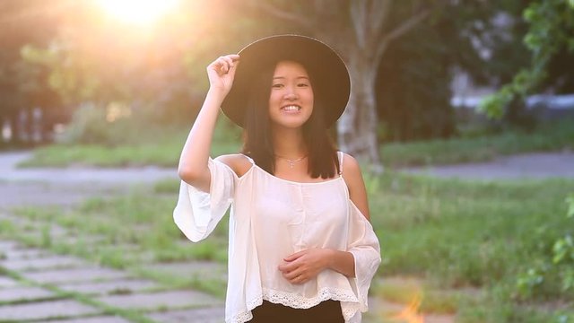 Eastern appearance with black straight hair. Cute female Young beautiful Asian girl in the green park background portrait, look to camera and showes tan, emotions hamming face