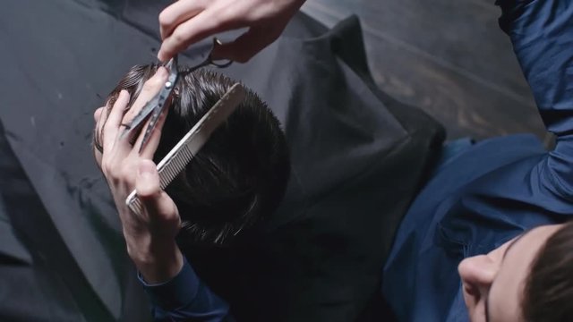 Top view of barber clipping wet hair with scissors while working on new haircut for man